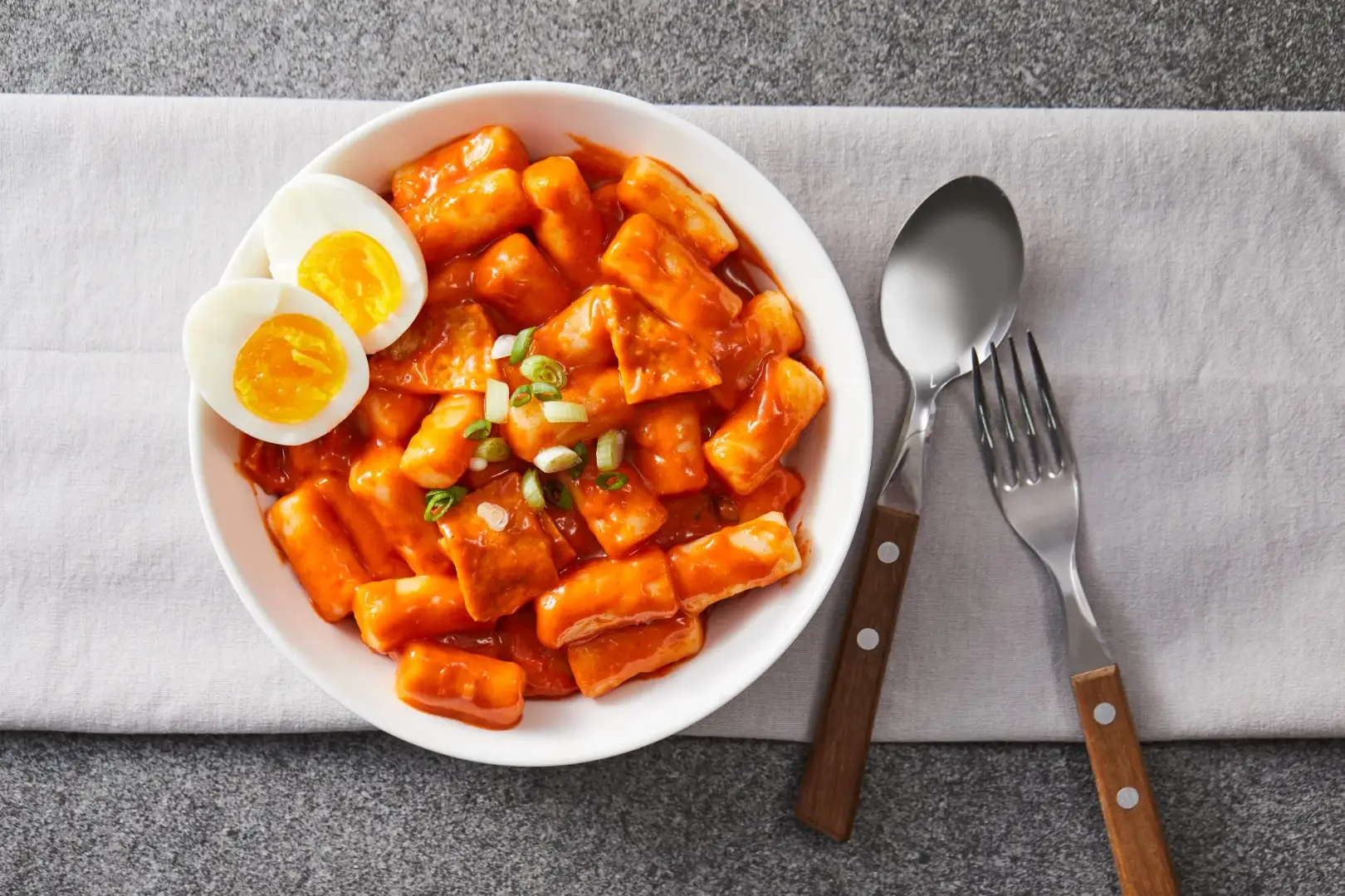 Authentic spicy tteokbokki Korean street food bowl with chewy rice cakes, gochujang sauce, boiled egg halves and green onion garnish ready to serve.