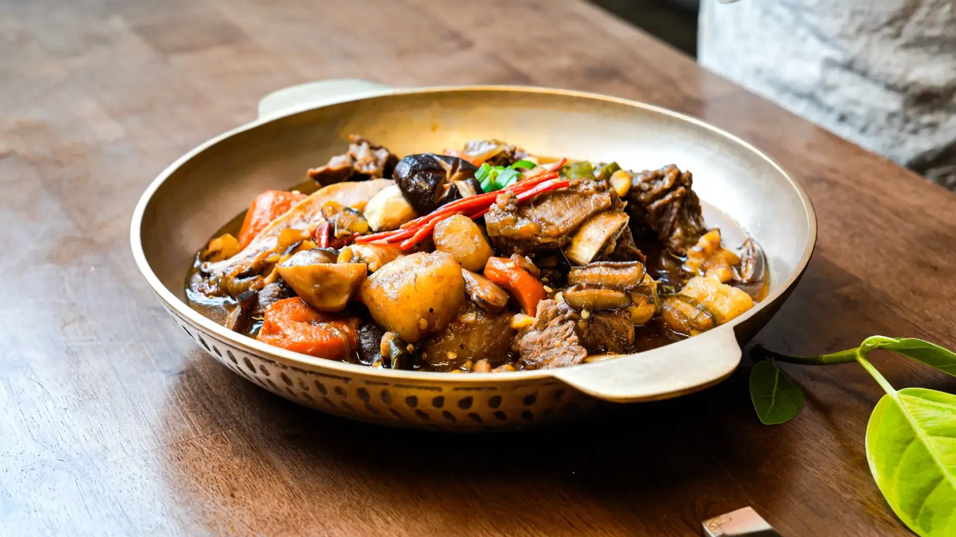 Traditional Korean braised short ribs galbijjim with tender beef, carrots and daikon radish in glossy soy-based sauce served in traditional Korean bronze bowl on wooden background.