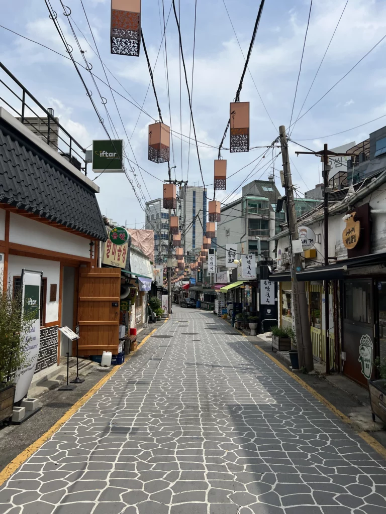 Traditional Seochon Hanok Village street in Seoul with authentic Korean restaurant signs and traditional tile-decorated overhead banners creating the historic dining district atmosphere near Giwajip.