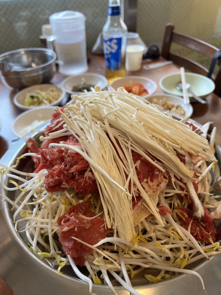 Traditional Korean bulgogi with beef and fresh bean sprouts cooking in a pan at Seochon Giwajip restaurant in Seoul with banchan side dishes and soju bottle.