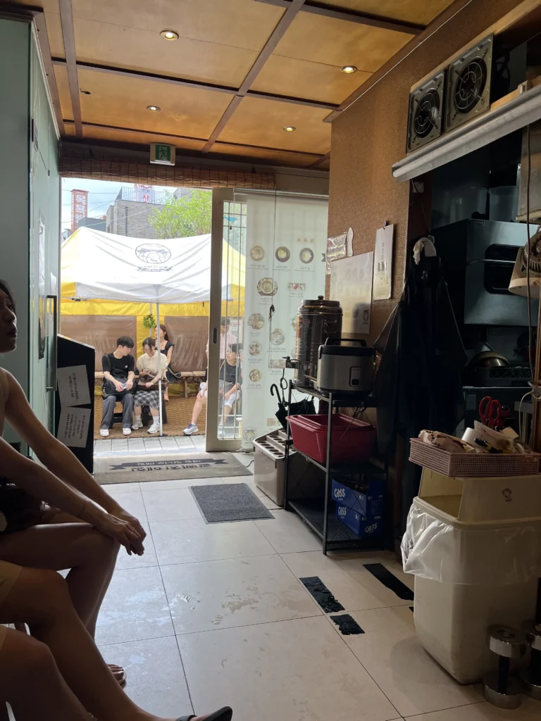 Interior view of Jalppaejin Memil Korean buckwheat restaurant kitchen area looking toward entrance with outdoor seating and customers dining in Seoul alley.