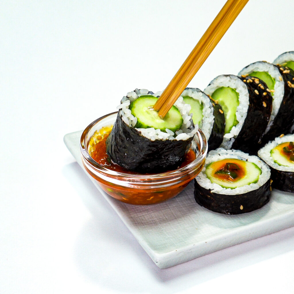 Rolled cucumber kimbap dipped in soy-based sauce, highlighting fresh flavor.