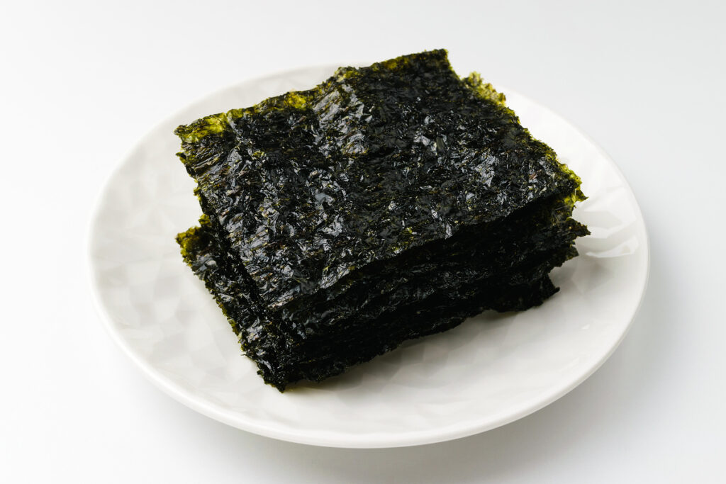 Stacked sheets of roasted Korean seaweed gim seasoned with sesame oil and salt on white plate for traditional Korean meal.