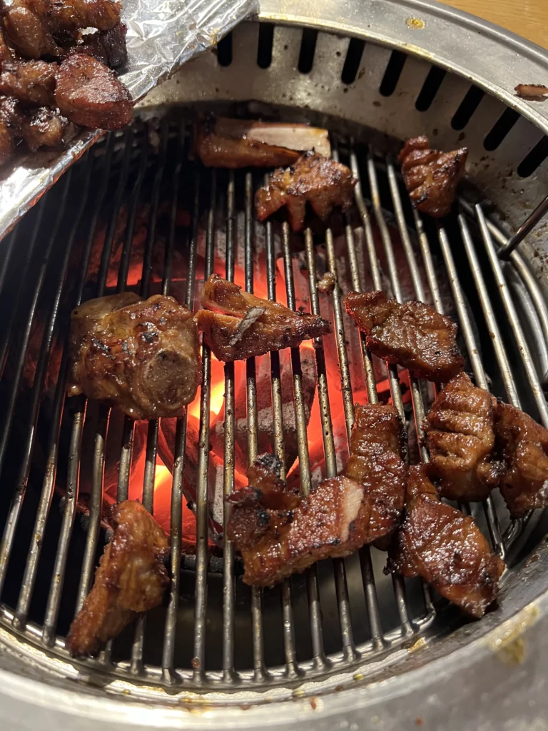 Sizzling dwaeji galbi Korean pork ribs with caramelized edges cooking over red-hot charcoal flames at Mapo Charcoal Pork Ribs.