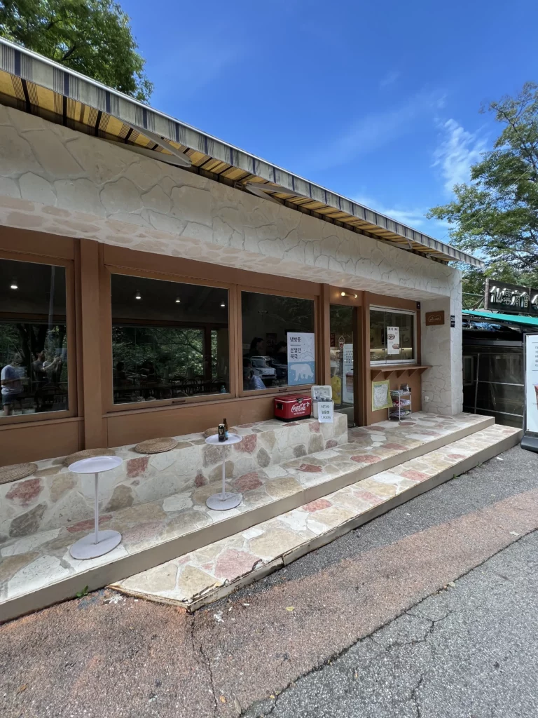 Exterior view of Bukhansan Lounge mountain view cafe with stone counter seating area, large windows, and natural surroundings at the entrance of Bukhansan National Park in Ui-dong Seoul.
