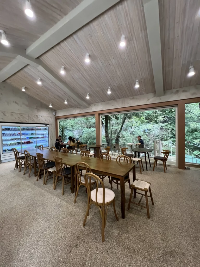 Spacious interior dining area of Bukhansan Lounge mountain view cafe with wooden communal tables, pendant lighting, and panoramic forest views through floor-to-ceiling windows at Bukhansan National Park in Seoul.