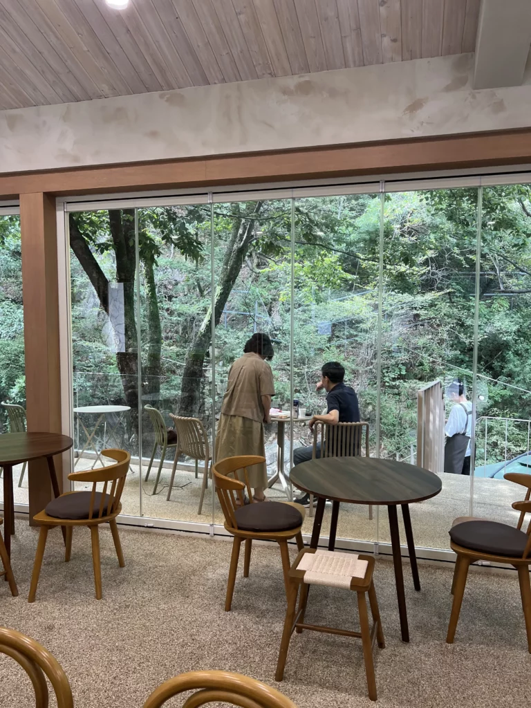Modern interior of Bukhansan Lounge mountain view cafe with wooden furniture and floor-to-ceiling windows overlooking lush forest scenery, featuring outdoor terrace seating with guests enjoying the natural Bukhansan National Park views in Ui-dong Seoul.