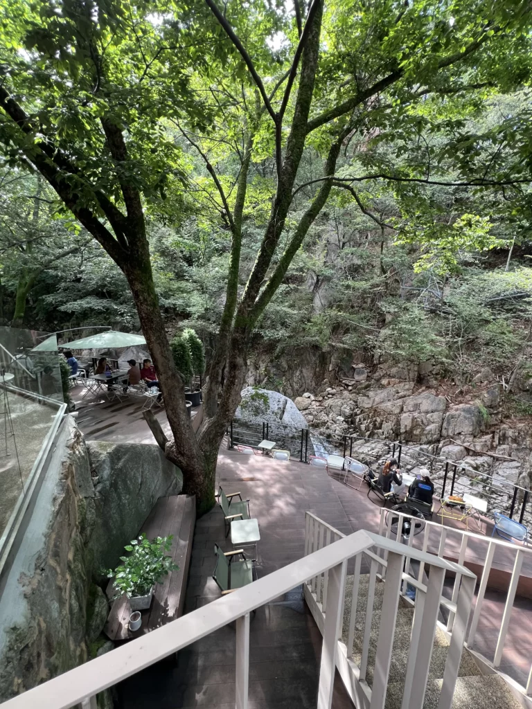 Multi-level outdoor terrace view at Bukhansan Lounge cafe featuring natural stone formations and mature trees, with multiple seating areas overlooking Ui-dong valley in Bukhansan National Park Seoul.