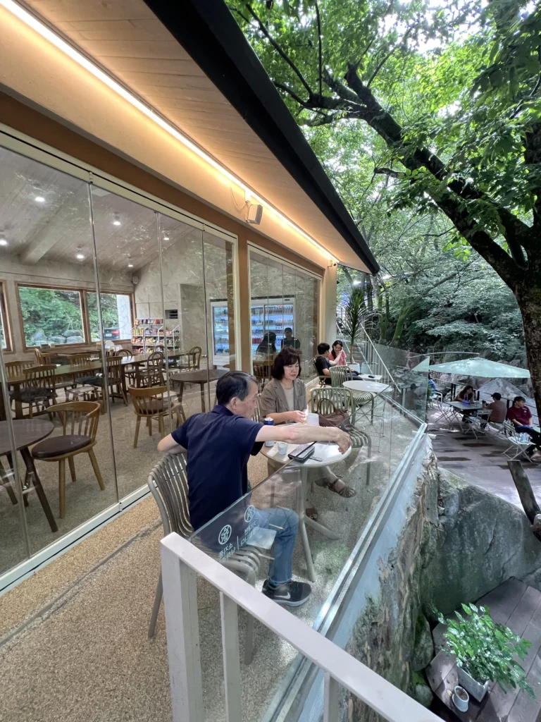 Guests enjoying outdoor terrace seating with glass railings at Bukhansan Lounge mountain view cafe, overlooking multi-level forest terraces and lush greenery at Bukhansan National Park in Ui-dong Seoul.