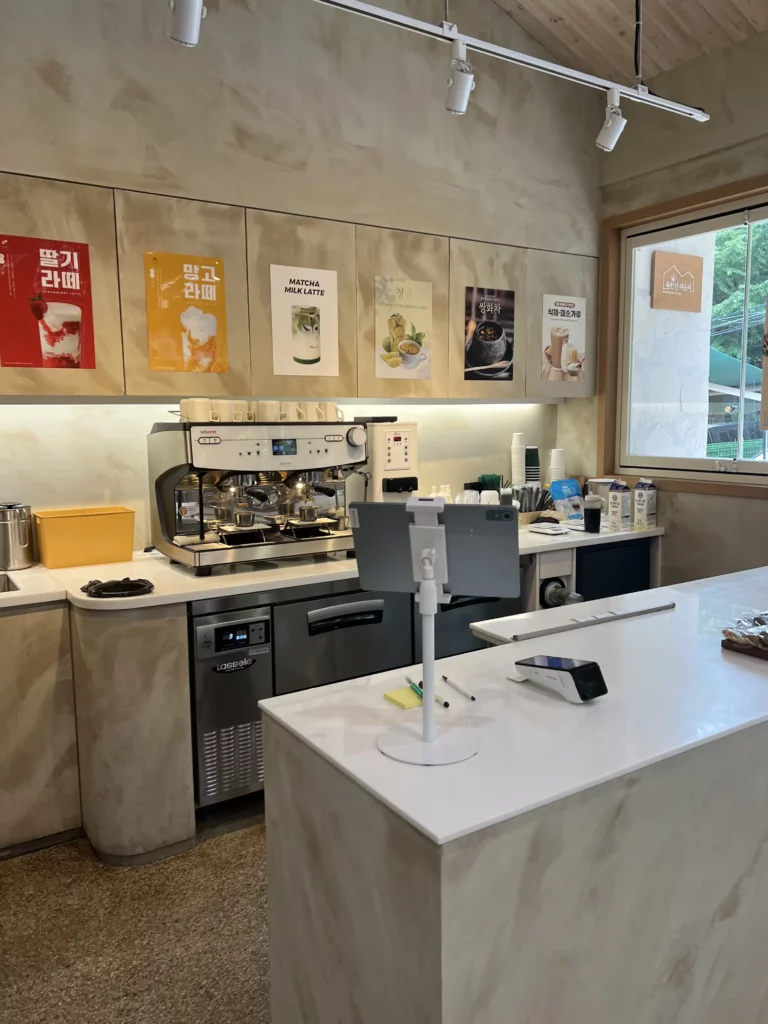 Coffee bar counter at Bukhansan Lounge with espresso machine, beverage menu posters, and barista equipment for serving specialty drinks at the mountain view cafe in Bukhansan National Park Seoul.