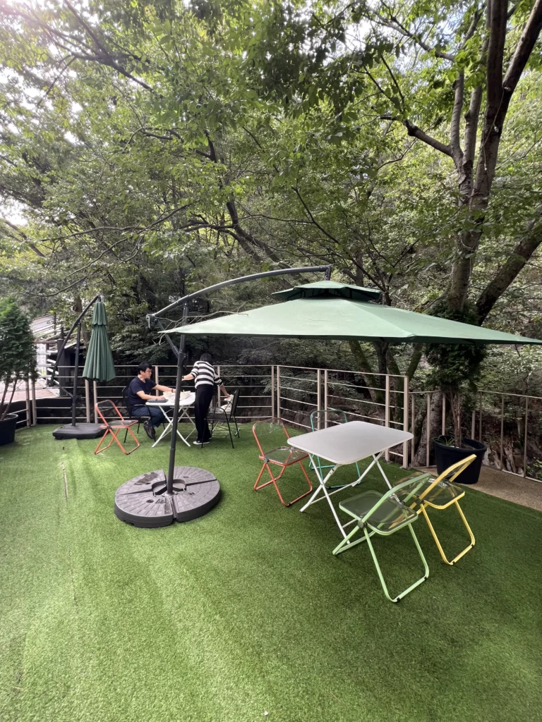 Outdoor rooftop terrace with artificial turf and colorful folding tables at Bukhansan Lounge cafe, featuring green umbrella shade and forest canopy views for post-hike relaxation at Bukhansan National Park in Seoul.