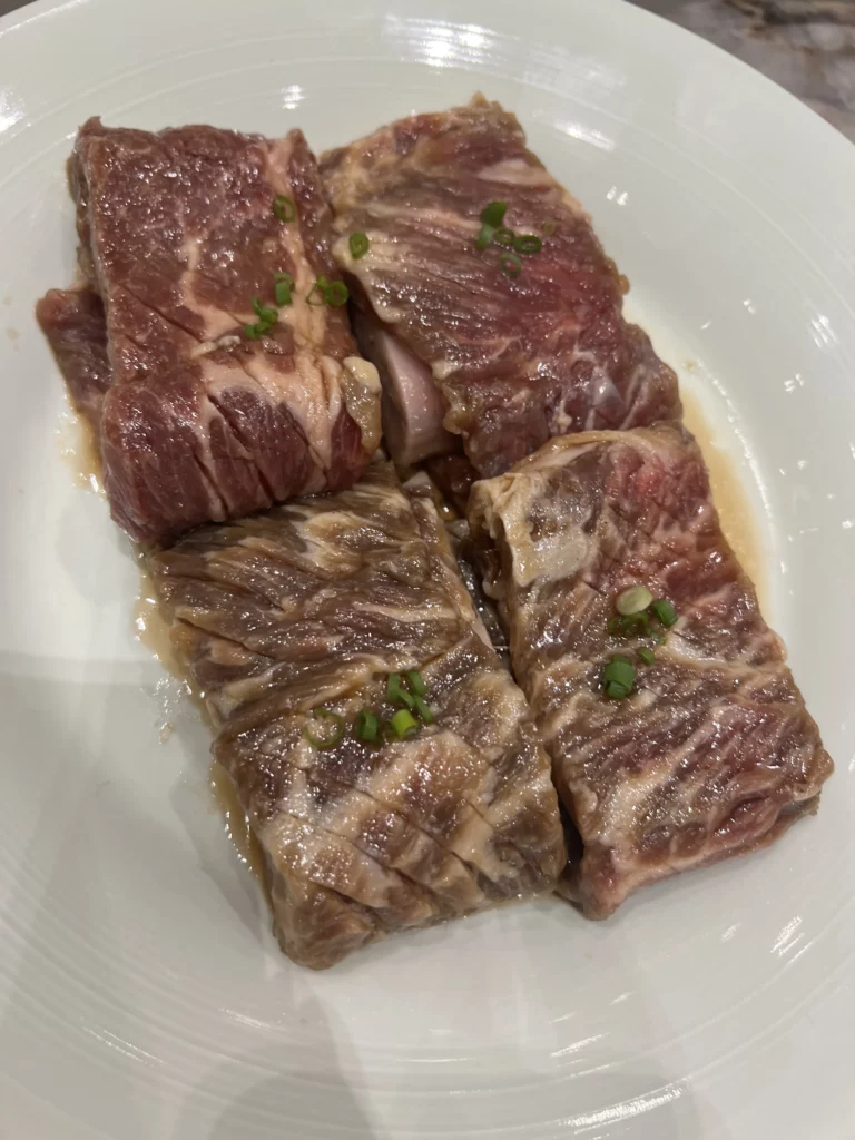 Marbled Hanwoo galbi beef short ribs garnished with green onions at Samwon Garden Seoul, showcasing premium Korean indigenous beef for traditional charcoal BBQ.