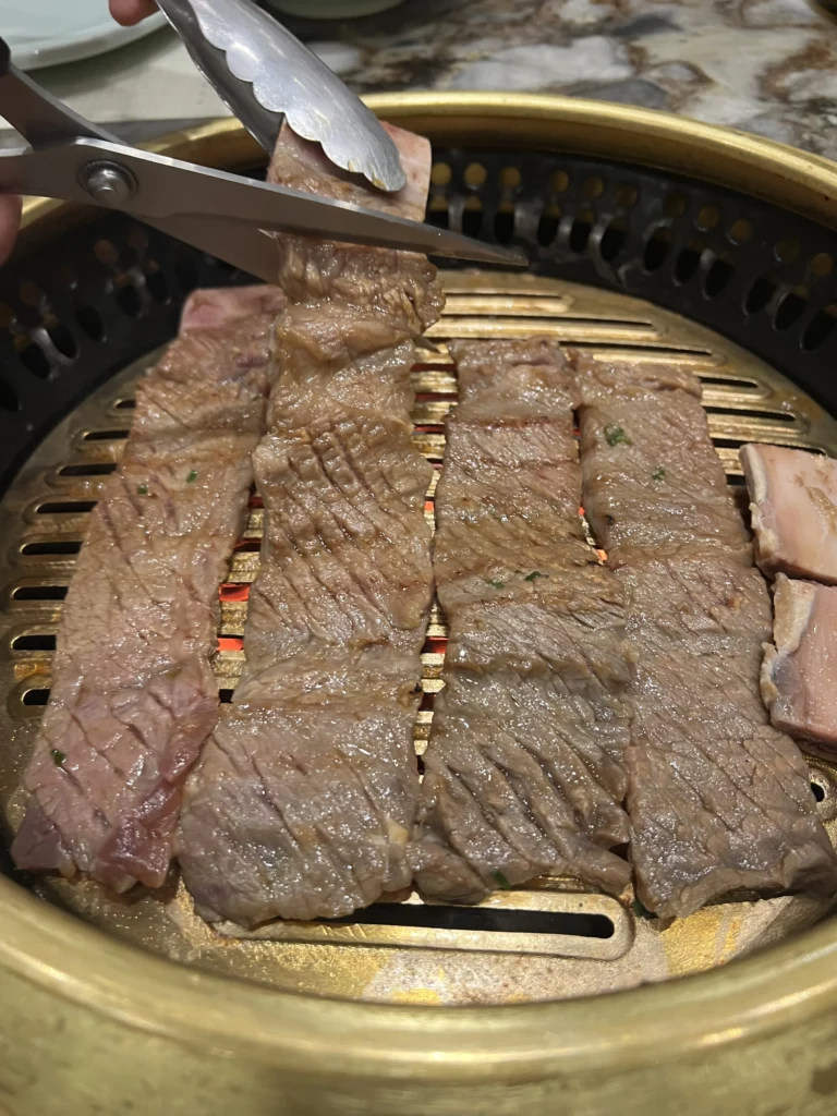 Grilling premium Hanwoo galbi beef short ribs with tongs on a charcoal BBQ grill at Samwon Garden Seoul, showing caramelized Korean beef with perfect grill marks.