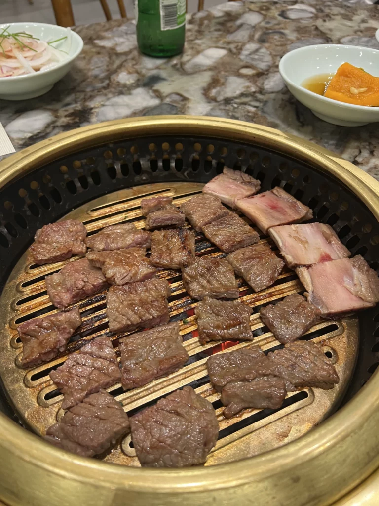 Perfectly grilled Hanwoo galbi beef short ribs on charcoal BBQ grill at Samwon Garden Seoul, served with traditional Korean banchan side dishes.