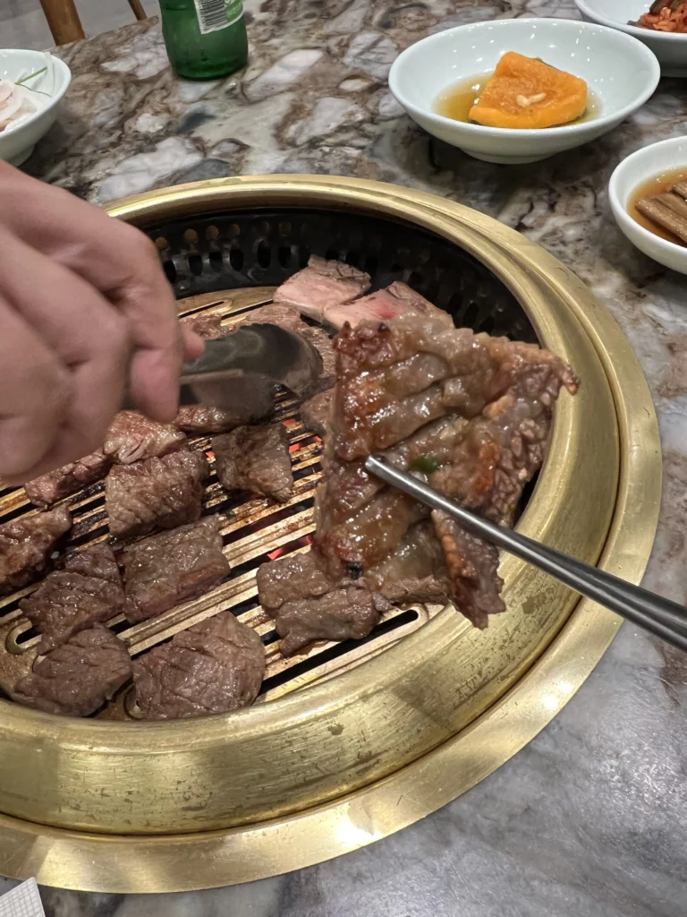 Cutting grilled Hanwoo galbi beef short ribs with scissors on charcoal BBQ grill at Samwon Garden Seoul, demonstrating traditional Korean BBQ dining technique.