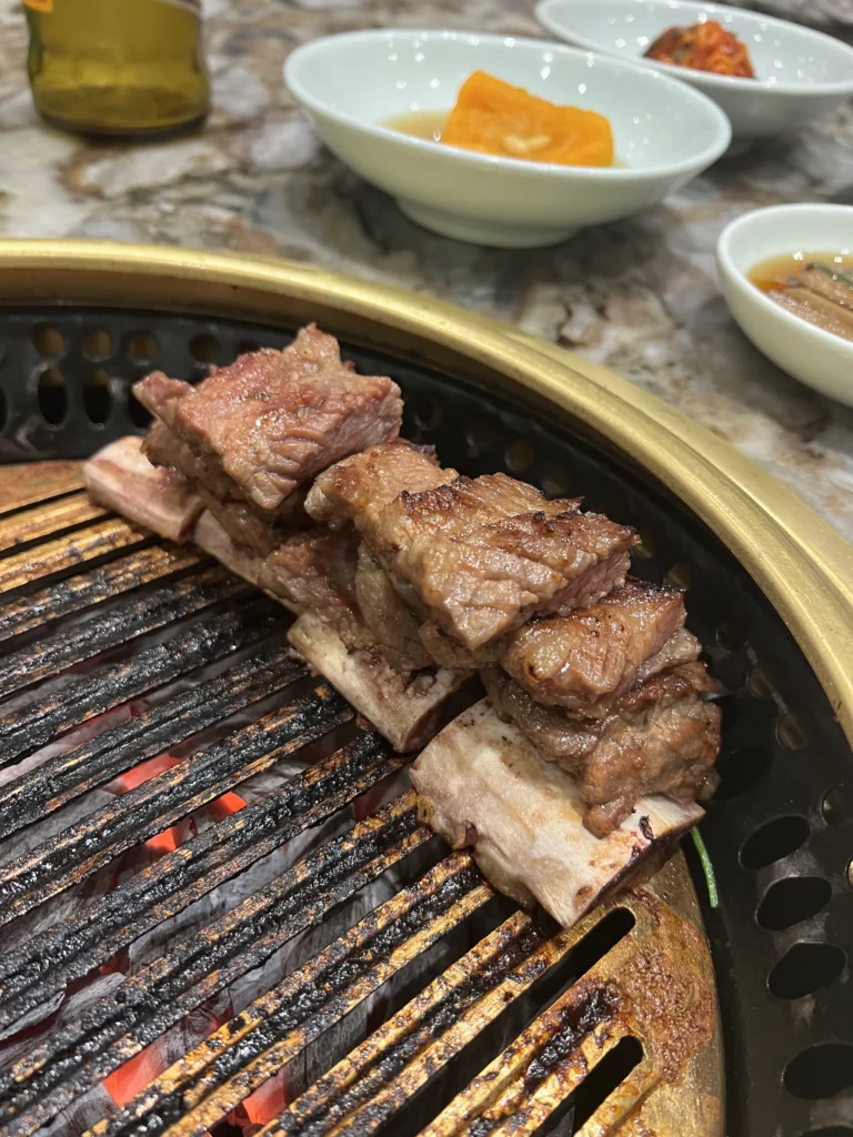 Premium Hanwoo galbi short ribs grilling over traditional charcoal at Samwon Garden Seoul with Korean BBQ side dishes and banchan.