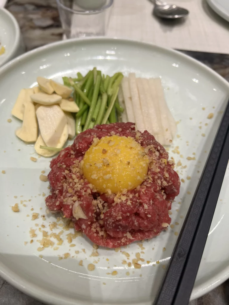 Premium Hanwoo beef tartare with raw egg yolk topped with pine nuts and served with fresh vegetables at Samwon Garden, Seoul's renowned Korean BBQ restaurant.
