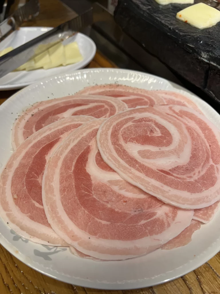 Premium raw samgyeopsal pork belly slices arranged in spiral pattern ready for stone grill cooking at Seokam Saeng Sogeum-gui Korean BBQ restaurant.