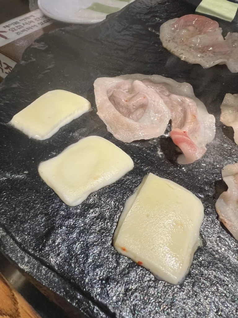 Fresh samgyeopsal pork belly and rice cakes grilling on patented volcanic stone cast iron grill plate at Seokam Saeng Sogeum-gui Korean BBQ restaurant.