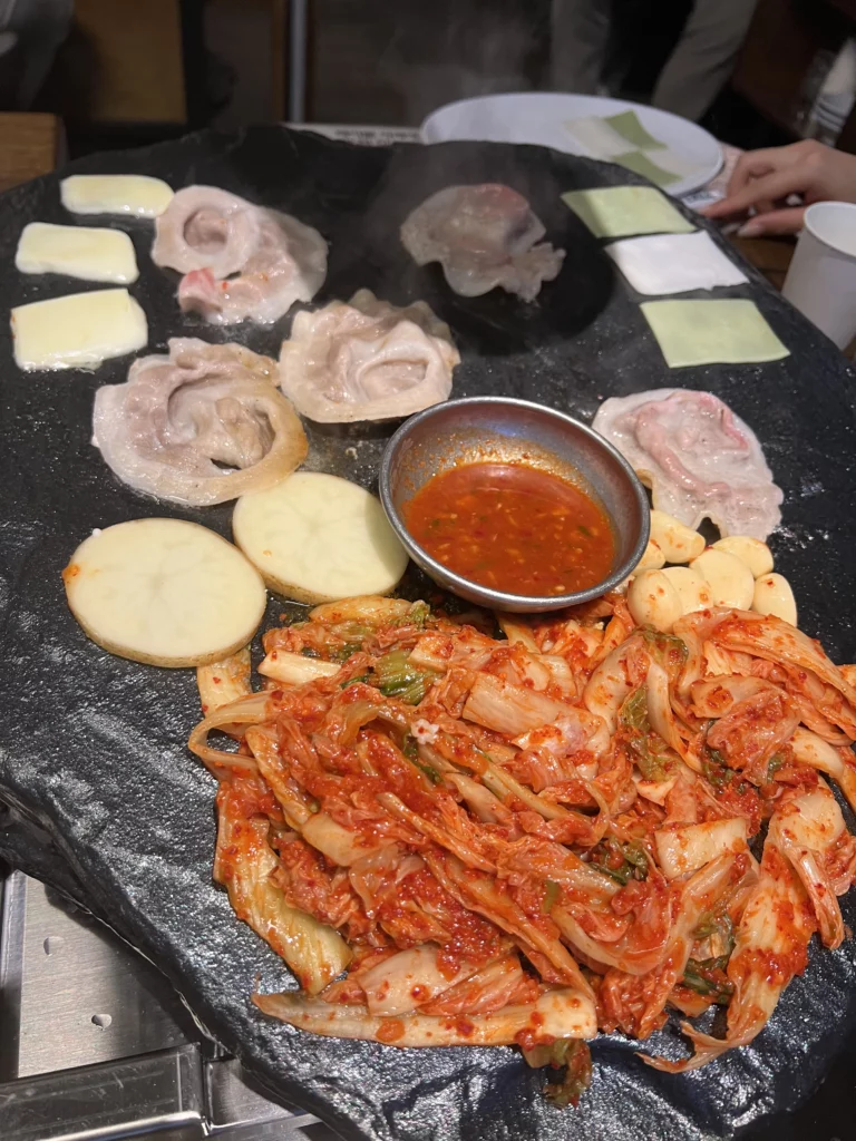 Signature Chungju apple kimchi with grilling samgyeopsal pork belly and rice cakes on volcanic stone grill plate at Seokam Saeng Sogeum-gui Korean BBQ Seoul.
