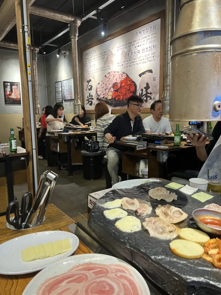 Interior dining room at Seokam restaurant showing guests grilling premium samgyeopsal pork belly on signature stone cast iron plates in Seoul.