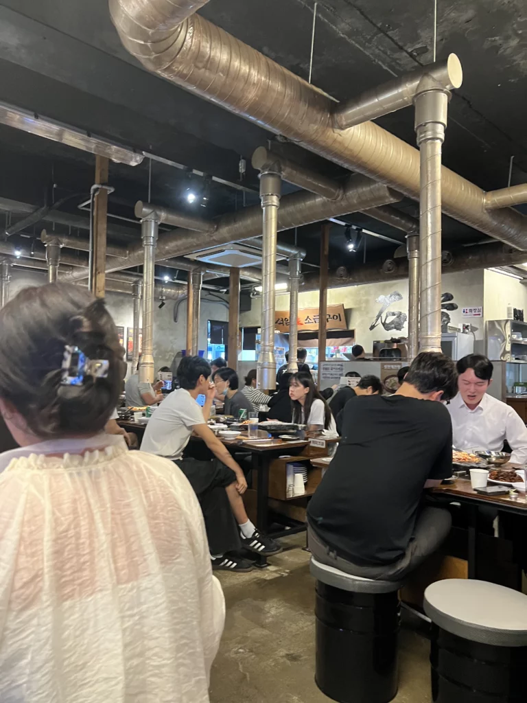 Diners enjoying premium samgyeopsal Korean BBQ at Seokam Saeng Sogeum-gui restaurant in Seoul with volcanic stone grill tables and industrial-style interior.