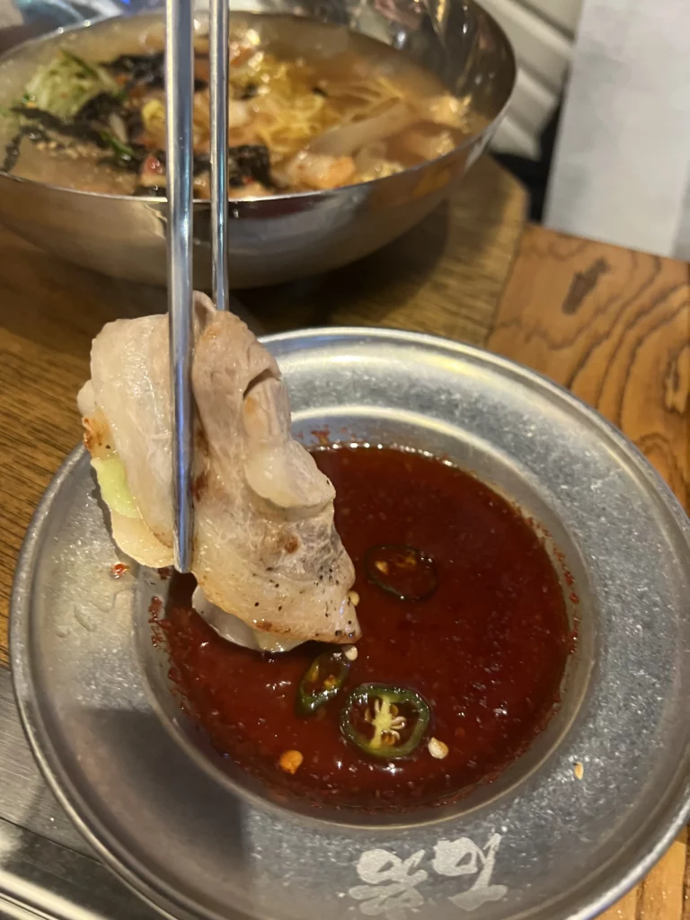 Grilled samgyeopsal pork belly being dipped in spicy sauce with jalapeño and garlic at Seokam Saeng Sogeum-gui Korean BBQ Seoul.