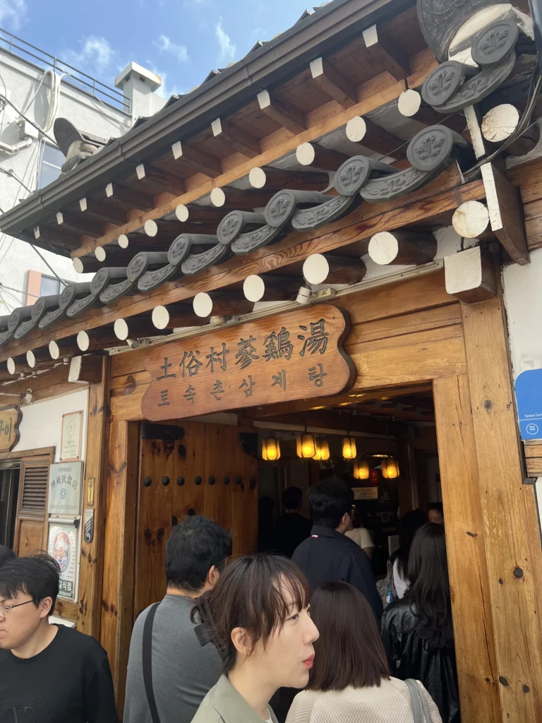 Tosokchon Samgyetang traditional hanok entrance with wooden signage and curved tile roof, visitors entering Seoul's legendary Korean ginseng chicken soup restaurant near Gyeongbokgung Palace.