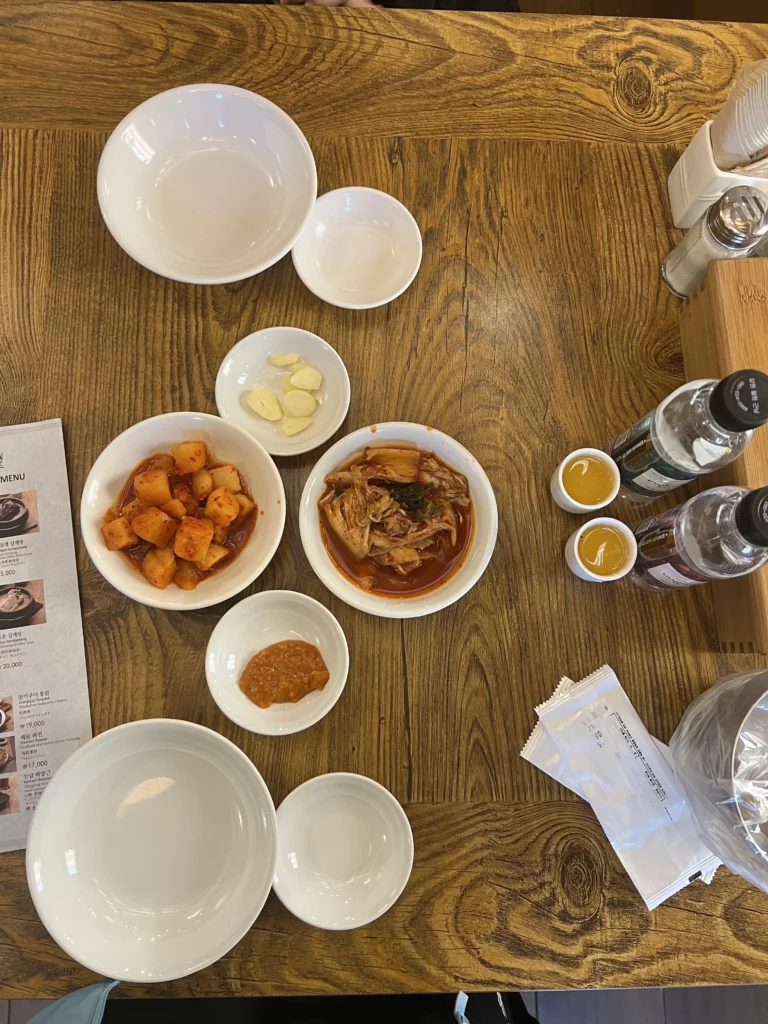 Table setting at Tosokchon with banchan side dishes, kimchi, kkakdugi radish, garlic, ginseng liquor, and empty bowls before samgyetang meal in Seoul.