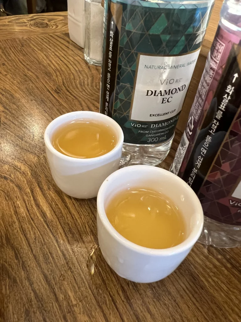 Complimentary ginseng liquor insam-ju served in white cups before samgyetang meal at Tosokchon restaurant, traditional Korean wellness dining custom in Seoul.