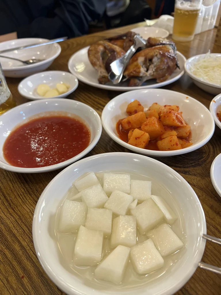 Korean side dishes banchan at Tosokchon including cubed radish mu, kkakdugi kimchi, and dipping sauce served with rotisserie chicken in Seoul.