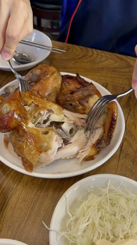 Tosokchon rotisserie chicken jingugui being pulled apart with forks showing tender juicy meat and crispy golden skin at Seoul's traditional Korean hanok restaurant near Gyeongbokgung Palace.