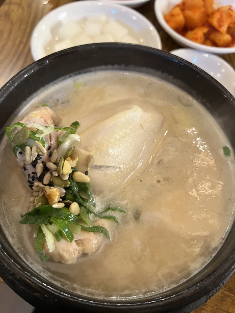 Tosokchon samgyetang served in traditional black earthenware pot with whole young chicken in milky pine nut broth, garnished with green onions and pine nuts, Seoul's legendary Korean ginseng chicken soup.