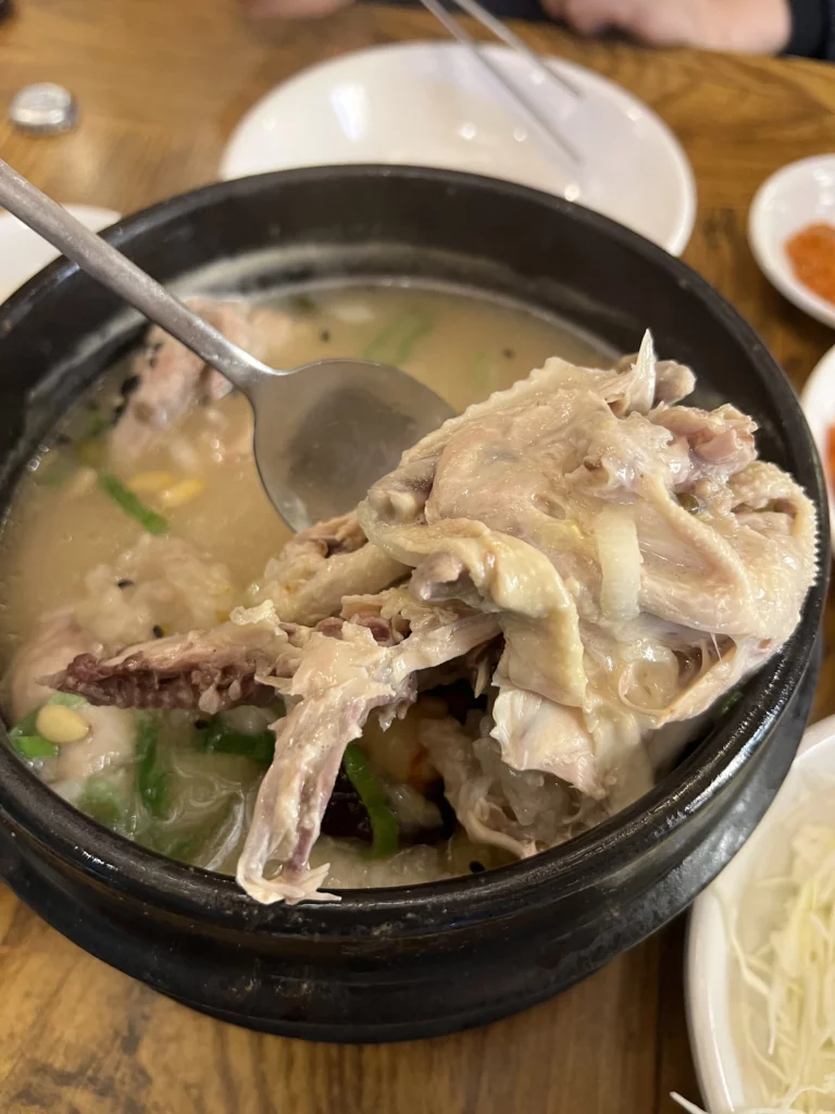Shredded tender chicken from Tosokchon samgyetang in ladle, showing fall-off-the-bone texture of Seoul's legendary Korean ginseng chicken soup.