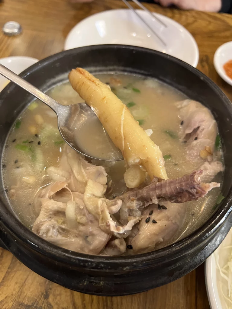 Whole Korean ginseng root from Tosokchon samgyetang held in spoon, key ingredient in Seoul's traditional ginseng chicken soup for wellness and energy.