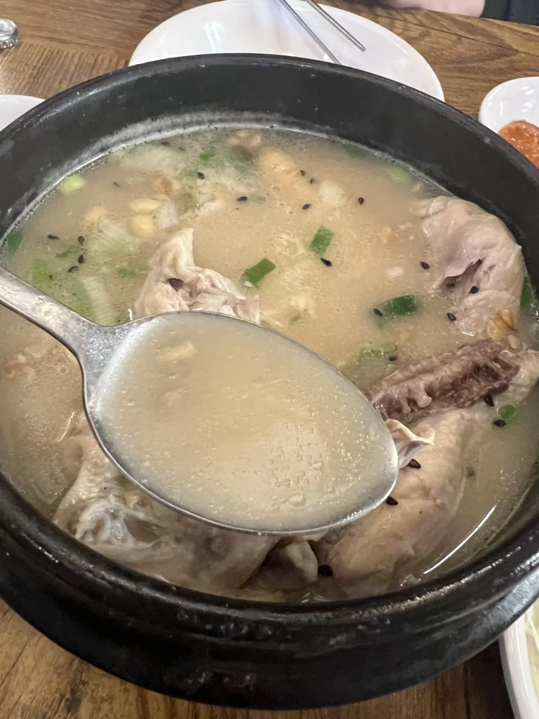 Creamy milky broth from Tosokchon samgyetang in spoon, signature pine nut and mung bean enriched Korean ginseng chicken soup in Seoul.