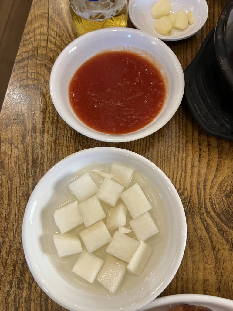 Korean side dishes banchan at Tosokchon including cubed radish mu in water and spicy gochujang dipping sauce with garlic, traditional accompaniments for Seoul's samgyetang and rotisserie chicken.