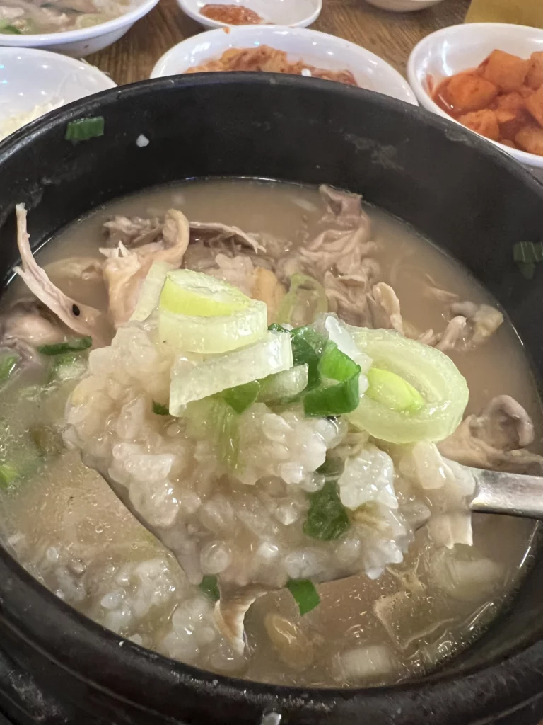 Glutinous rice from Tosokchon samgyetang mixed with creamy pine nut broth and green onions in spoon, traditional way to enjoy Korean ginseng chicken soup stuffing in Seoul.