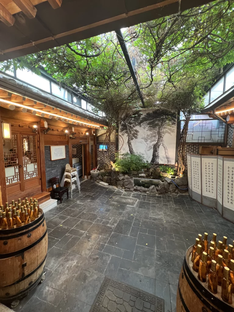 Traditional hanok courtyard garden at Tosokchon Samgyetang with stone flooring, central tree, and wooden barrels displaying ginseng liquor bottles, connecting multiple dining rooms in Seoul's legendary Korean ginseng chicken soup restaurant.