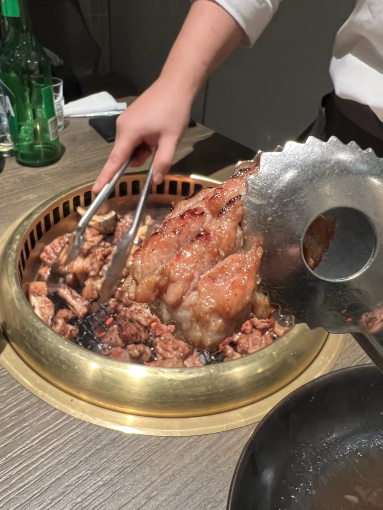 Tableside charcoal-grilled pork ribs being served with tongs at Bongpiyang Michelin Bib Gourmand Korean BBQ restaurant in Seoul.