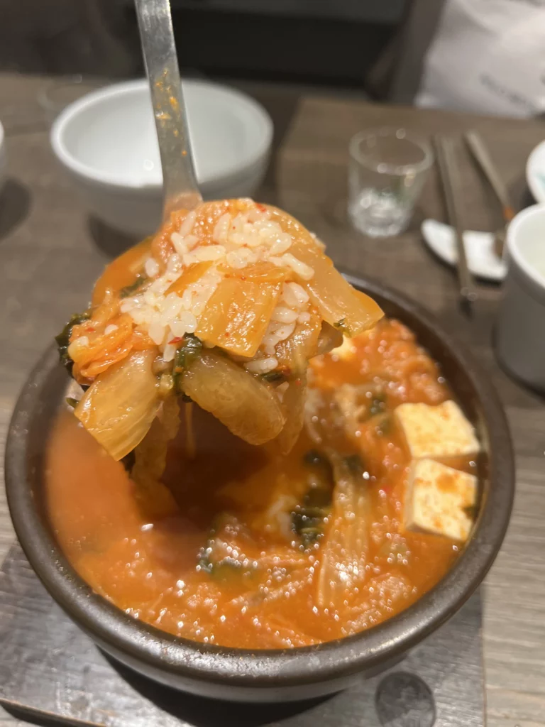 Rice and kimchi jjigae with tofu on spoon at Bongpiyang Michelin-recommended Korean BBQ restaurant in Seoul.