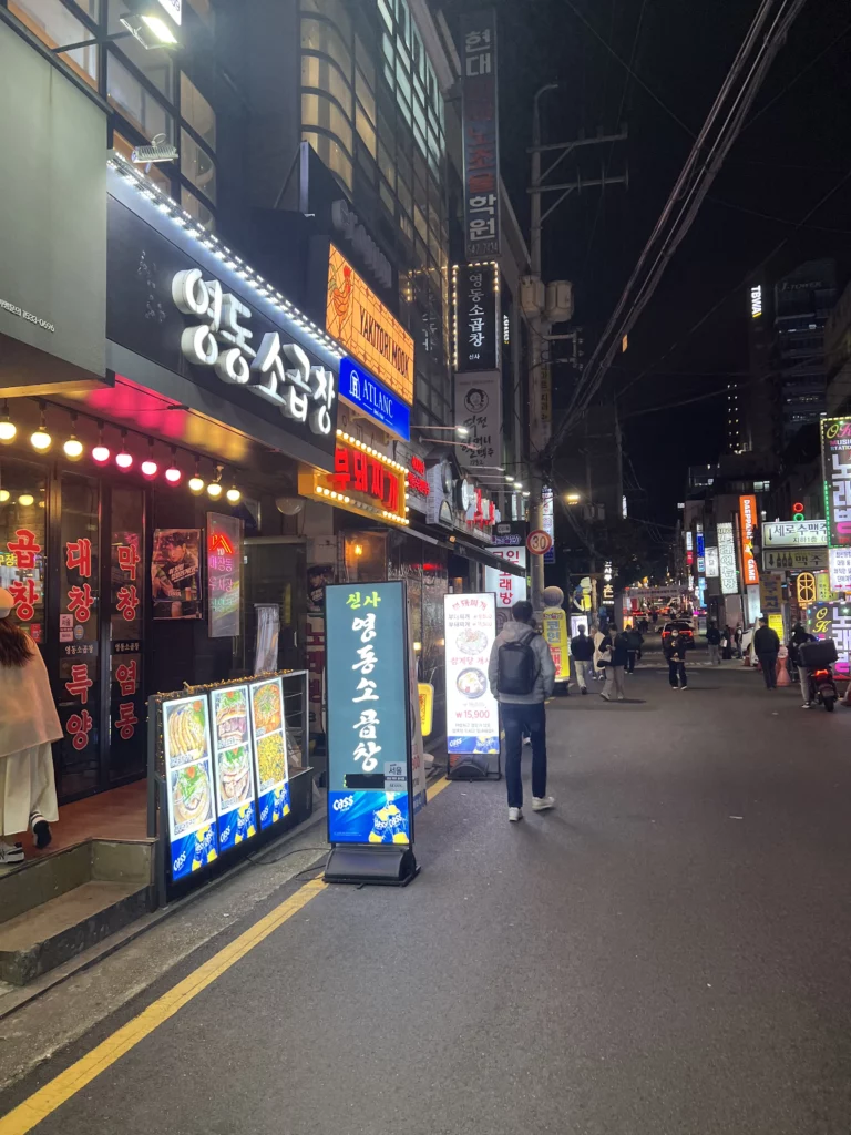 Night street view of Sinsa-dong neighborhood in Gangnam Seoul with illuminated Korean restaurant signs near Haega Jjukkumi authentic jjukkumi dining area.