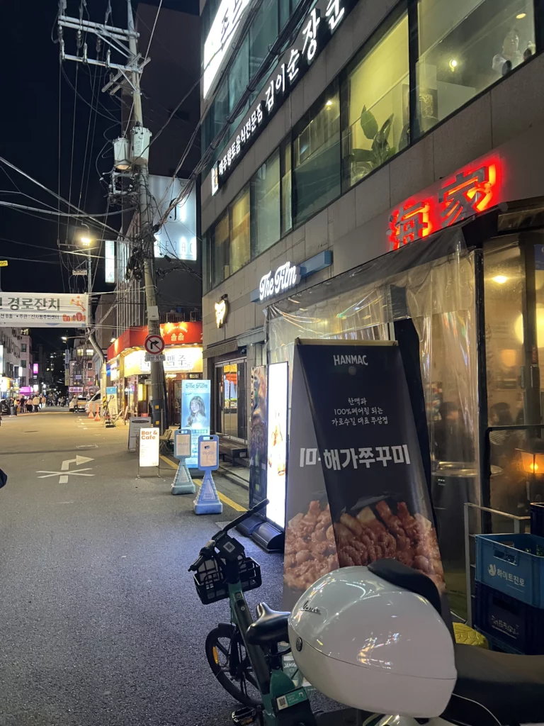 Haega Jjukkumi restaurant exterior with illuminated red neon signage at night in Sinsa-dong Gangnam, Seoul, featuring street view and menu display board for authentic Korean webfoot octopus jjukkumi dining.