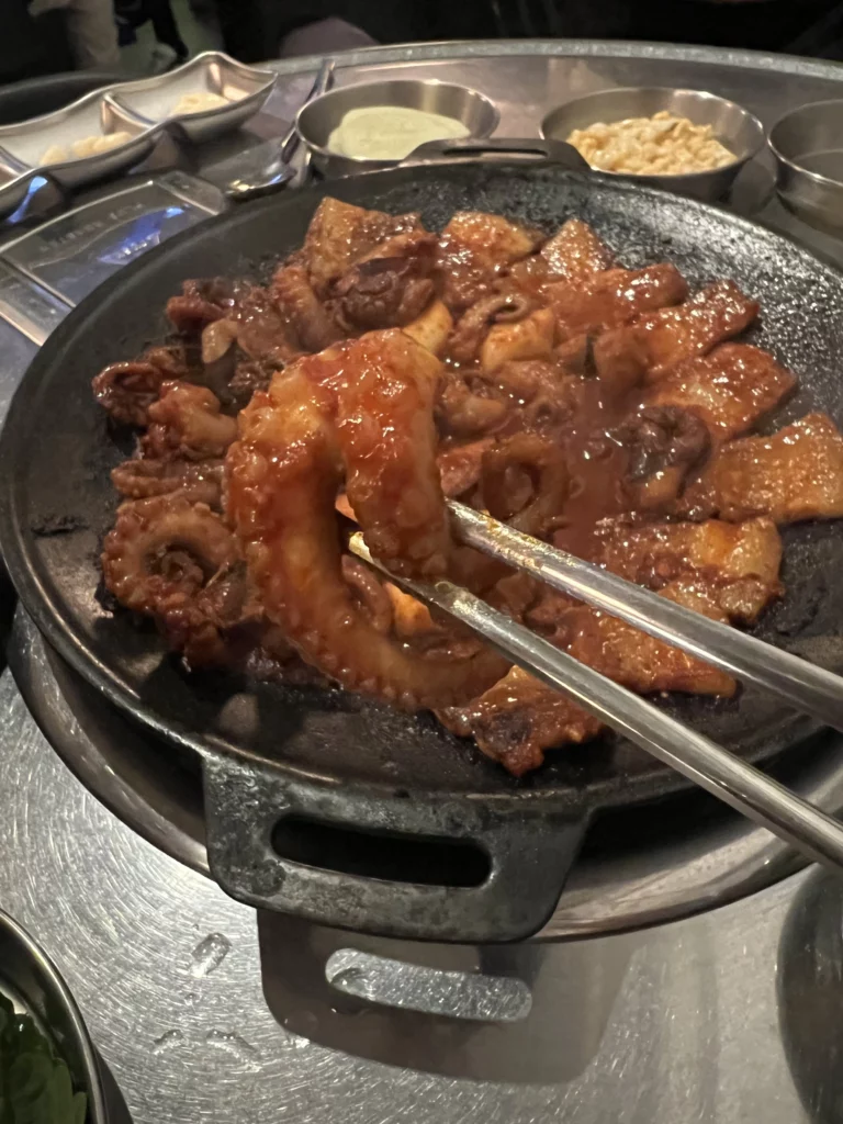 Grilled jjukkumi webfoot octopus and samgyeopsal pork belly in spicy gochujang marinade on black iron plate at Haega Jjukkumi restaurant Seoul.
