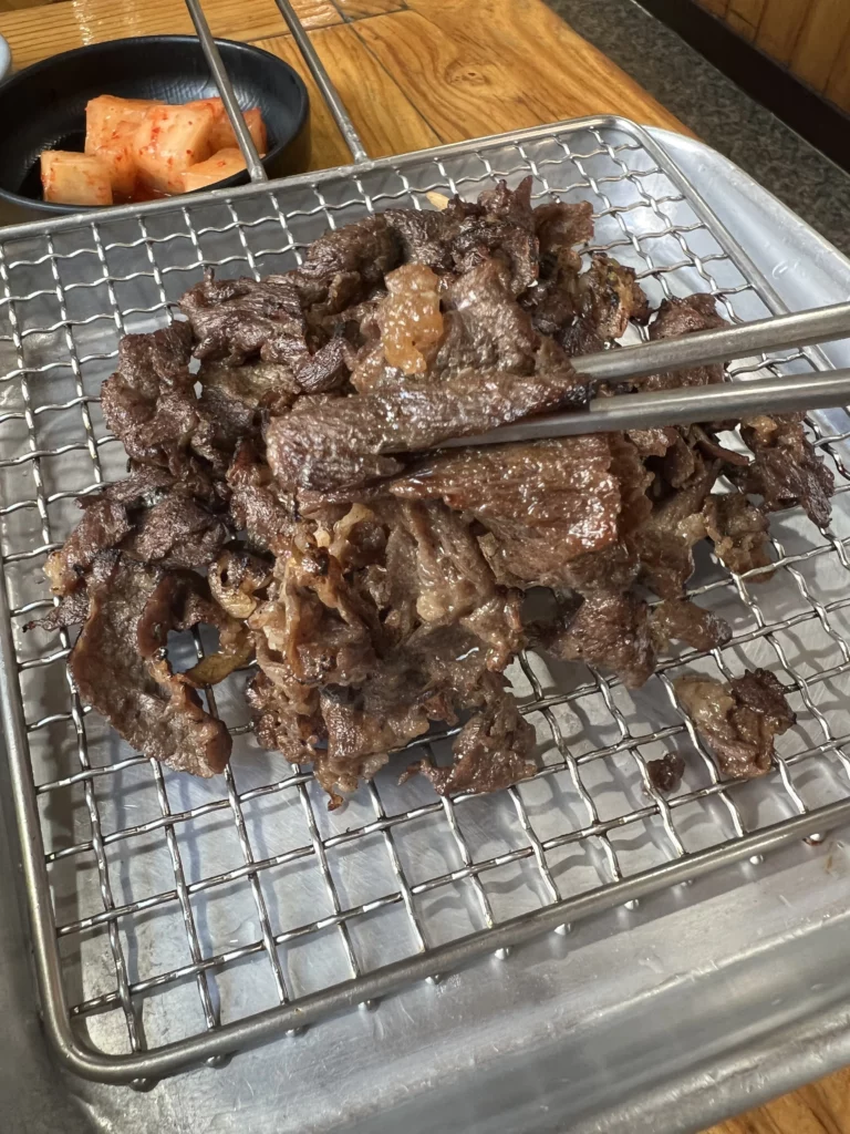 Seoksoebulgogi Korean marinated beef grilling on traditional stone grill at Nunnamu-jip restaurant with kimchi banchan side dishes.
