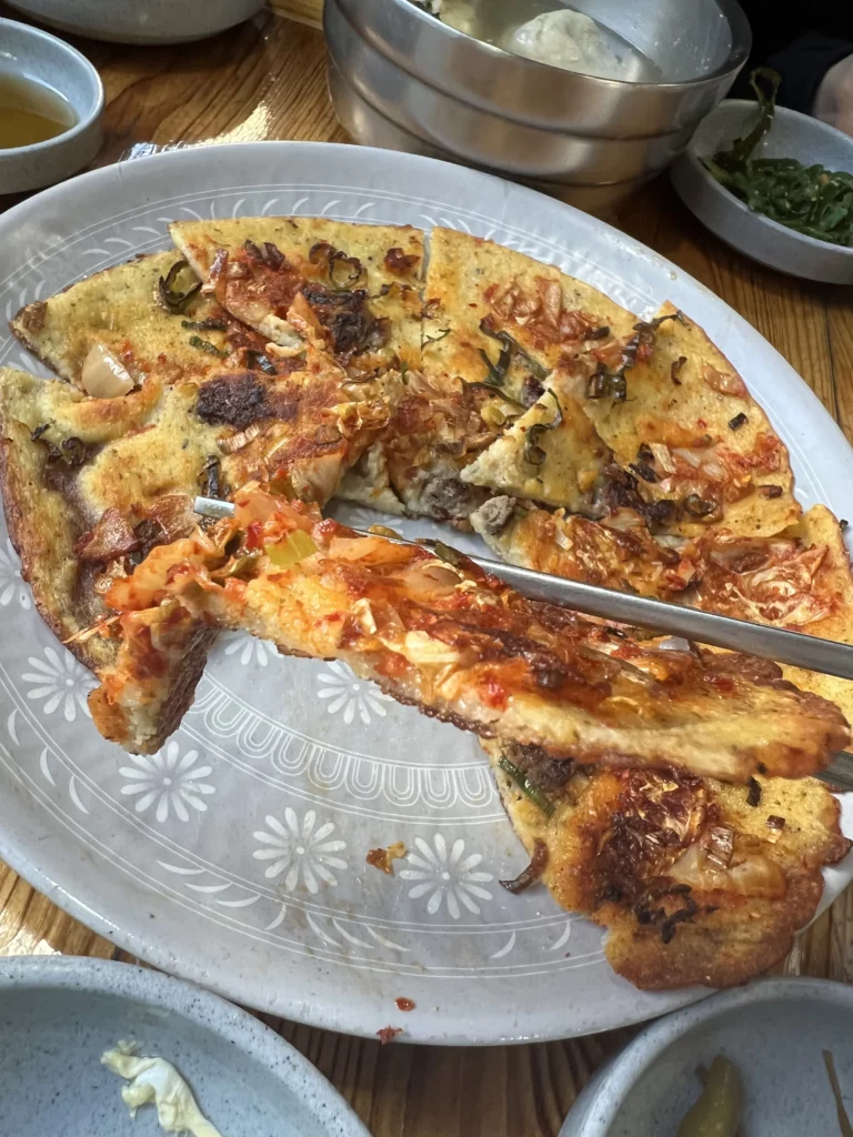 Crispy nokdu-bindaetteok Korean mung bean pancake sliced and served at Nunnamu-jip Bukchon restaurant Seoul with kimchi and vegetables.