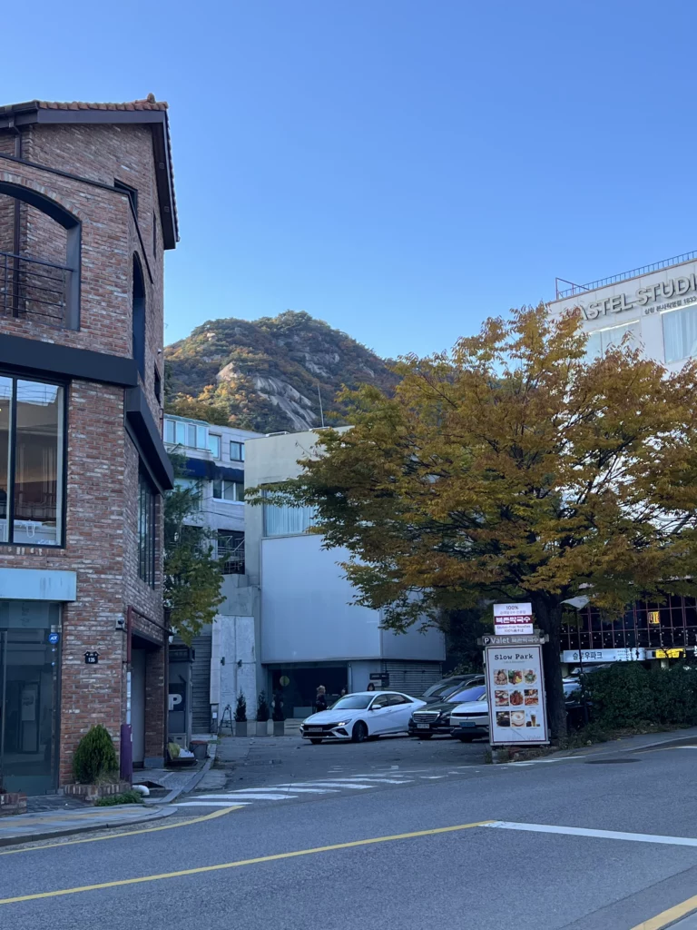 Bukchon Samcheong-dong neighborhood street view near Nunnamu-jip restaurant with Seoul mountain backdrop and modern architecture.
