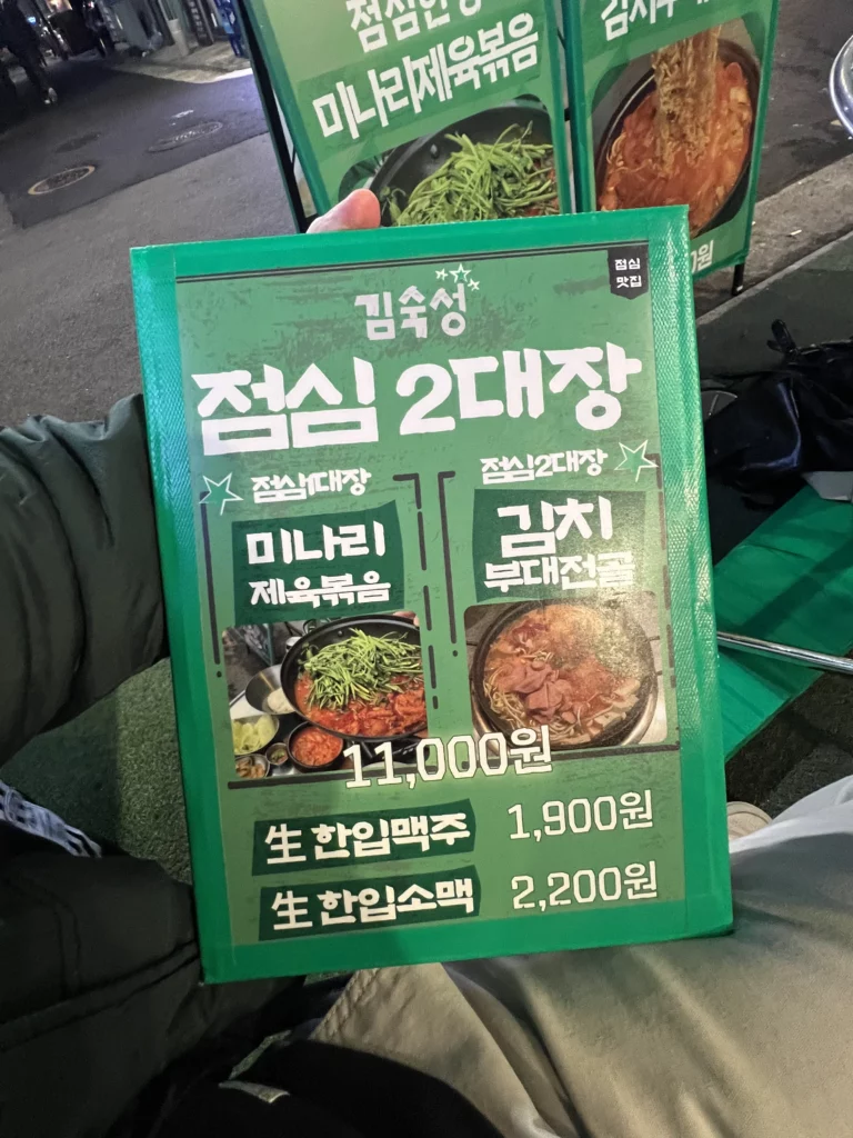 Lunch menu board at Gimsukseoung restaurant in Seoul displaying minari jaeyuk bokkeum and kimchi stew alongside 22-day aged samgyeopsal options with pricing.