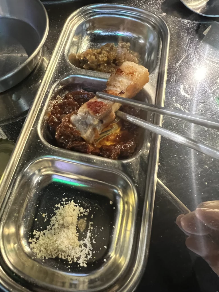 Grilled 22-day aged samgyeopsal being dipped in traditional Korean BBQ condiments at Gimsukseoung restaurant in Seoul.