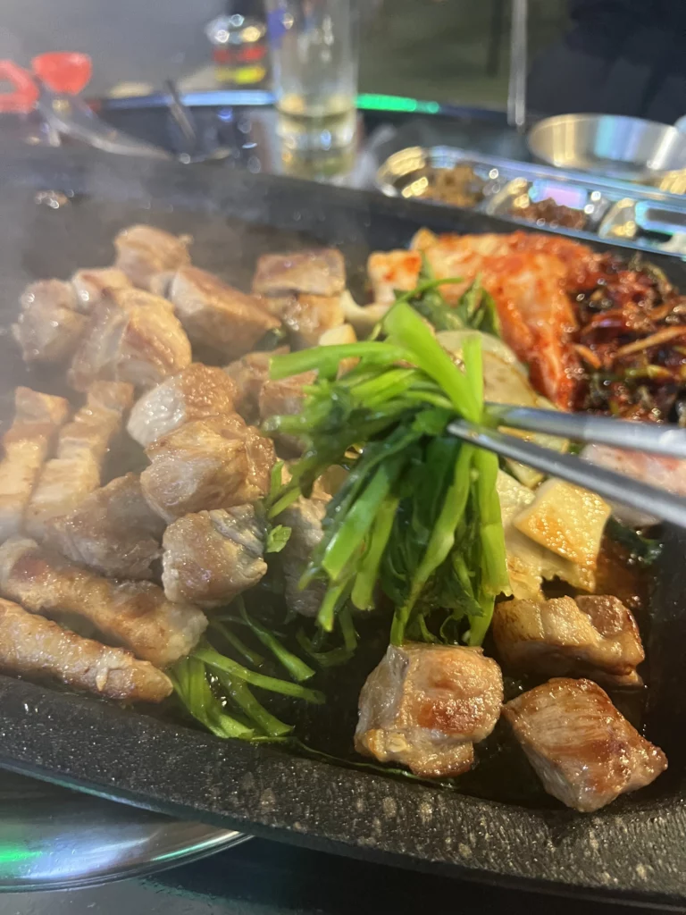 Grilled 22-day aged samgyeopsal with fresh minari vegetables and kimchi on a Korean BBQ grill at Gimsukseoung restaurant in Seoul.
